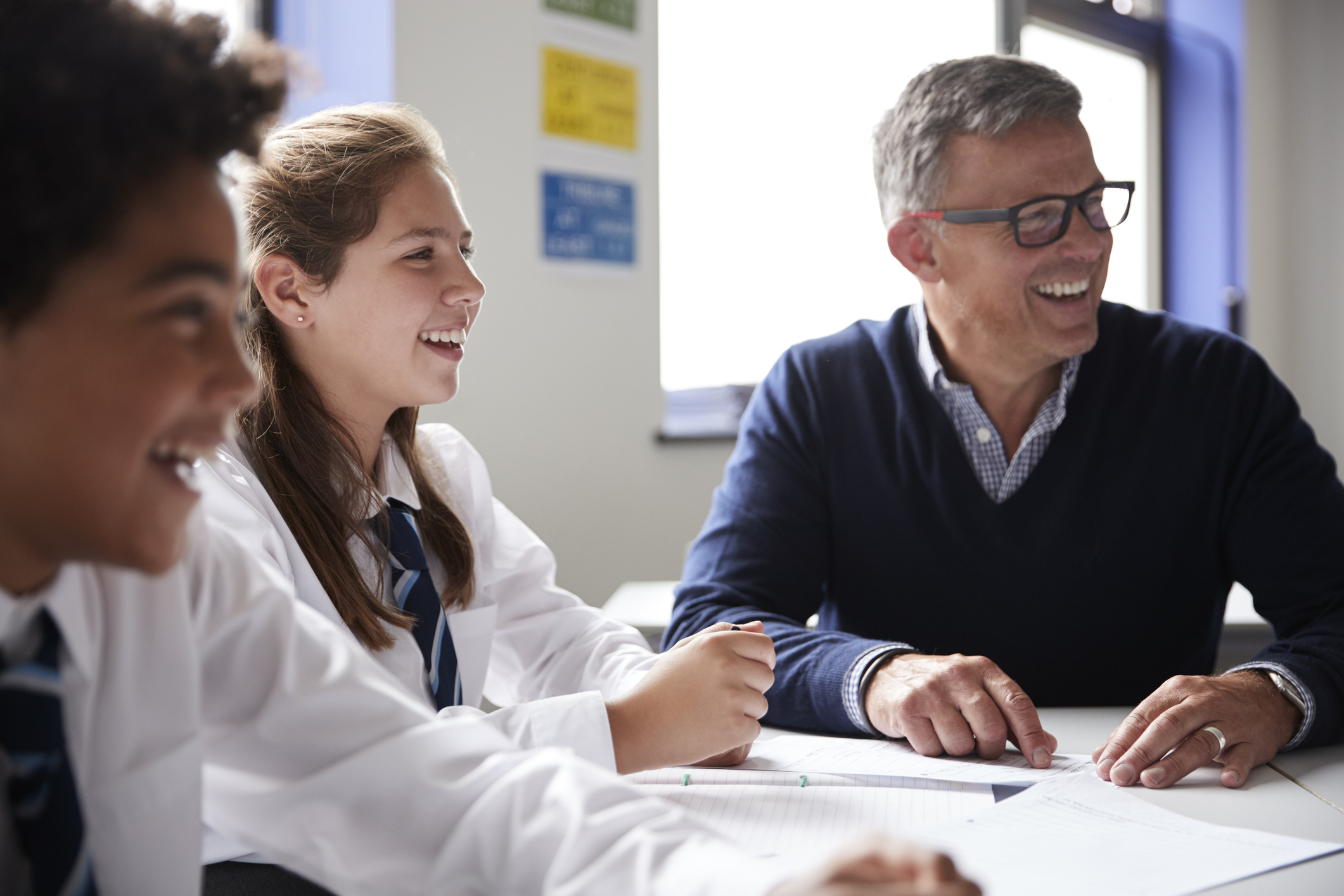 Male High School Tutor Sitting At Table With Students Teaching Lesson